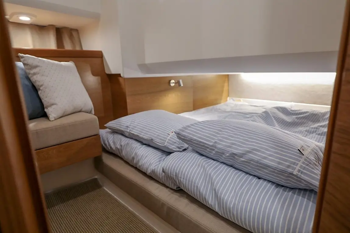 Cozy boat cabin featuring a cushioned seating area and neatly made twin beds with blue striped bedding and soft pillows.